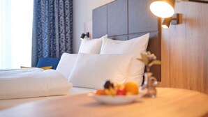 A hotel room with a neatly made bed, a bedside table with fruit, and a wall-mounted lamp. - Kucher's Genuss & Businesshotel (Darscheid)