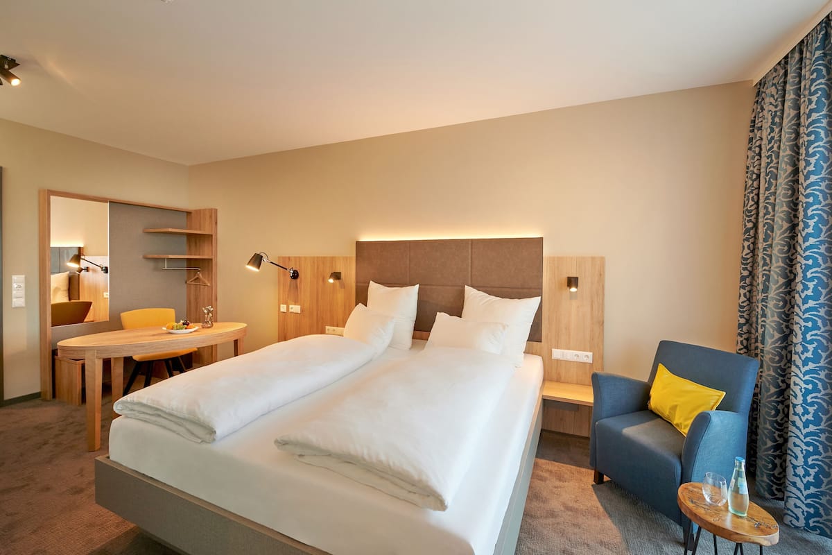 Une chambre d’hôtel avec un grand lit, un bureau, une chaise et une petite table sur laquelle se trouvent une bouteille et un verre.