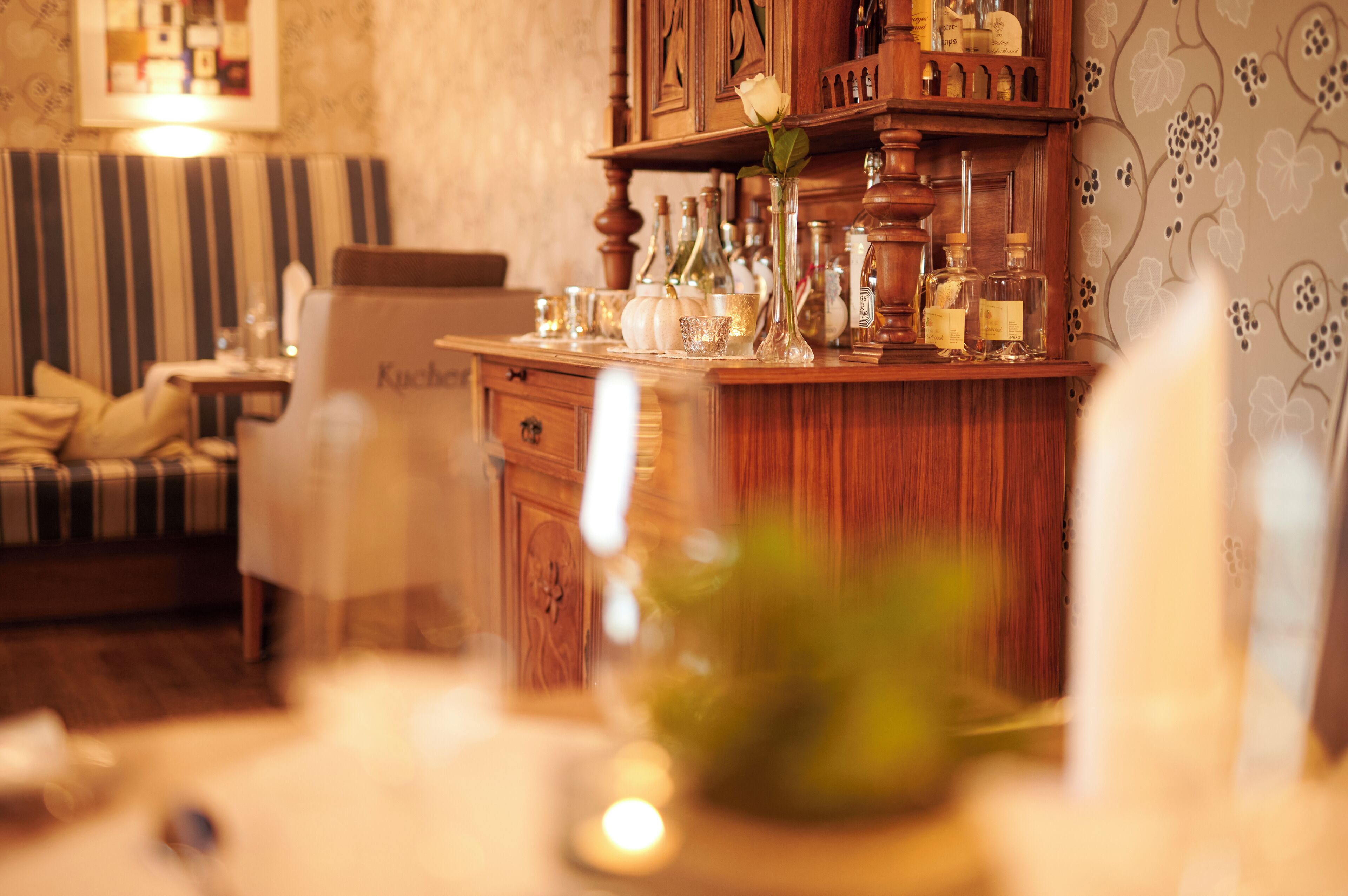 A cozy room with a wooden cabinet, a striped sofa, and a table with various bottles and a vase.