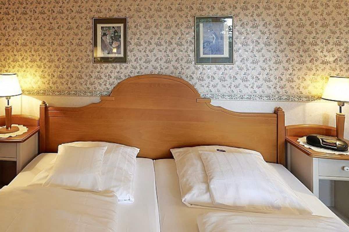 Un lit double avec deux oreillers, une tête de lit en bois, deux tables de chevet avec des lampes et un papier peint à motifs floraux.