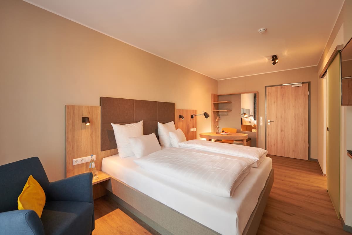 Une chambre d’hôtel avec un grand lit, des tables de chevet, une chaise, un bureau et un miroir.