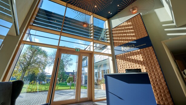 A modern hotel lobby with large glass doors, a reception desk, and a ceiling with a unique radial light fixture. - Kucher's Genuss & Businesshotel (Darscheid)