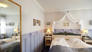 Habitación de hotel con dos camas, un espejo grande, mesitas de noche con lámparas y una cama con dosel.