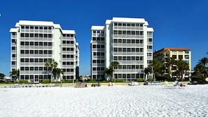A beachfront hotel with multiple floors, balconies, and a sandy beach area with sun loungers. - Spectacular Beach View! Right on Beach! Amazing views from all rooms! Sleeps 6 (Siesta Key)