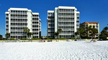 A beachfront hotel with multiple floors, balconies, and a sandy beach area with sun loungers.