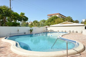 A swimming pool with a curved edge, surrounded by a tiled deck and a white wall.