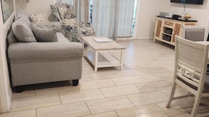 A living room with a grey sofa, a coffee table, a TV, and a cabinet. - Spectacular Beach View! Right on Beach! Amazing views from all rooms! Sleeps 6 (Siesta Key)