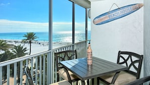 A balcony with a table and chairs, overlooking a beach. A bottle of wine is on the table. - Spectacular Beach View! Right on Beach! Amazing views from all rooms! Sleeps 6 (Siesta Key)