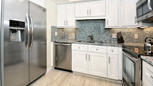 A modern kitchen with white cabinets, a stainless steel refrigerator, a dishwasher, a sink with a mosaic backsplash, and a microwave. - Spectacular Beach View! Right on Beach! Amazing views from all rooms! Sleeps 6 (Siesta Key)