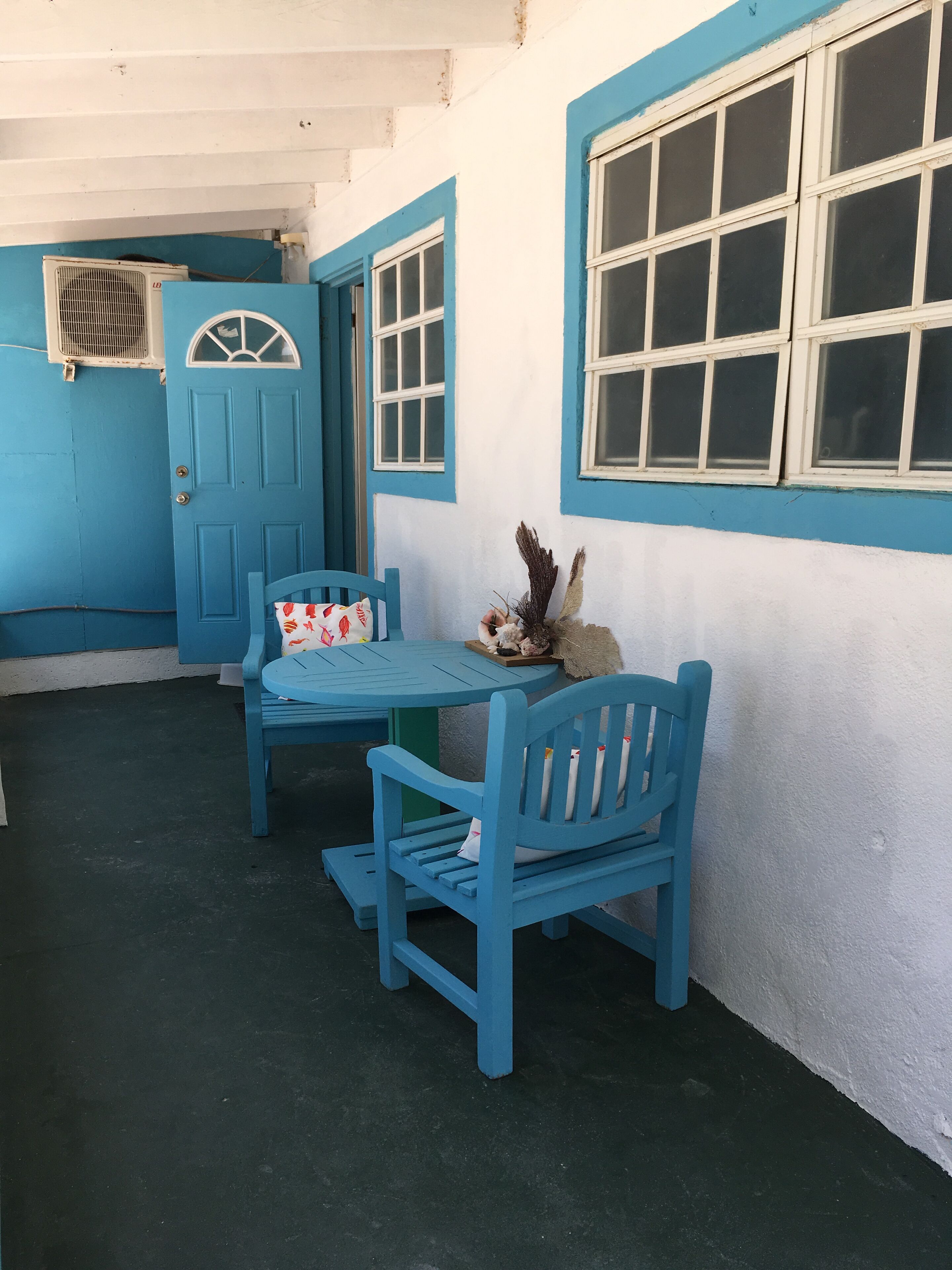 A room with a blue door, a window with white frames, and a table with a chair.