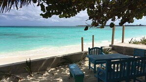 Un espace aménagé près de la plage, avec une table et des chaises, un banc et une vue sur l’océan turquoise.