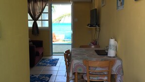 Un coin repas avec une table et des chaises, un ventilateur de plafond et une vue sur l’océan par une porte.