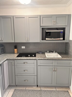 A kitchen with grey cabinets, a black microwave, a sink, and a granite countertop. - Perfect Beachfront Rental with Beautiful Views! (Steventon)