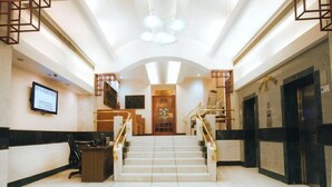 Vestíbulo de hotel con recepción, una escalera y un piso de baldosas con estampado de estrellas.