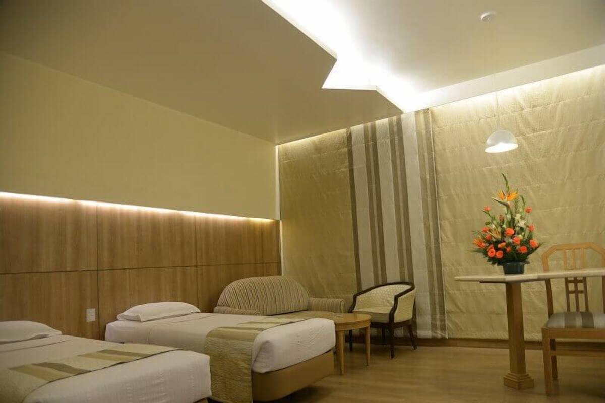 A hotel room with two single beds, a small table with a chair, and a decorative flower arrangement.