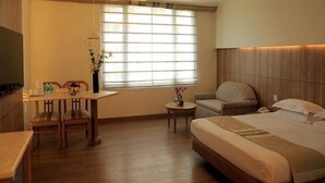Habitación de hotel con cama, escritorio, silla, mesita y ventana con persianas.