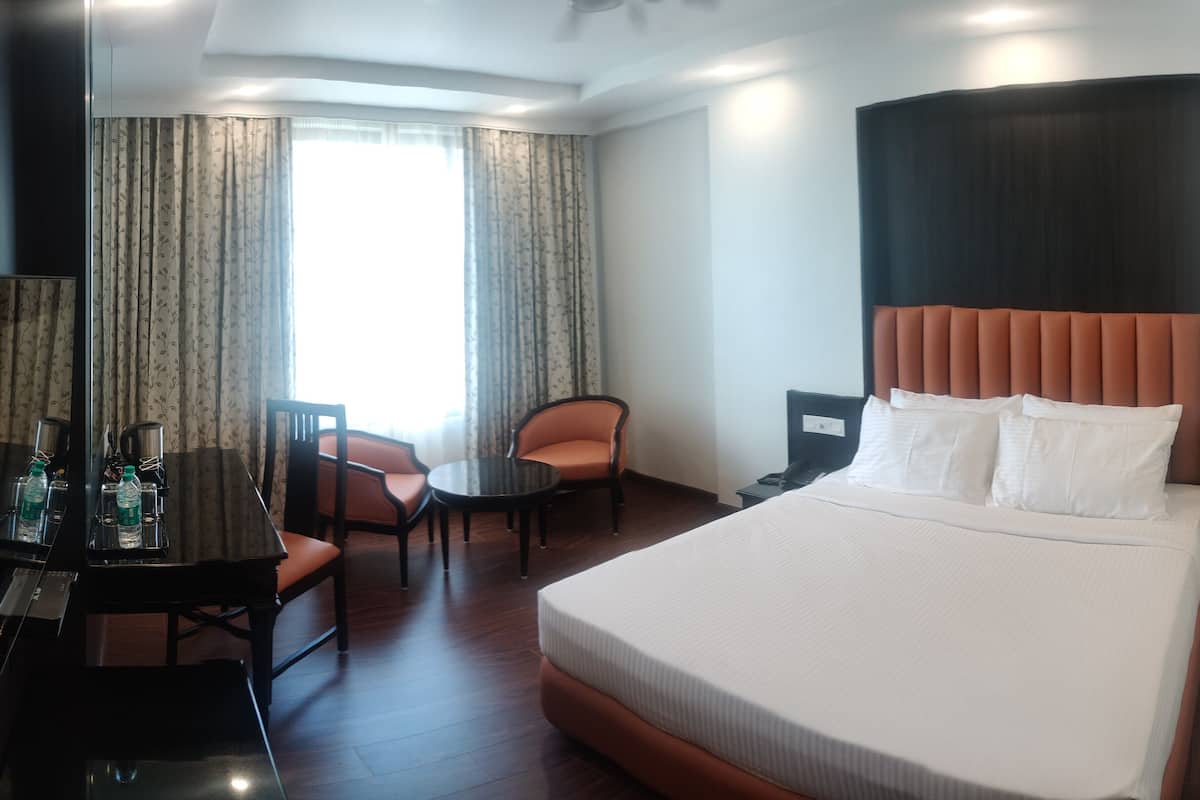 A hotel room with a large bed, a desk with a chair, a small table, and a sofa.