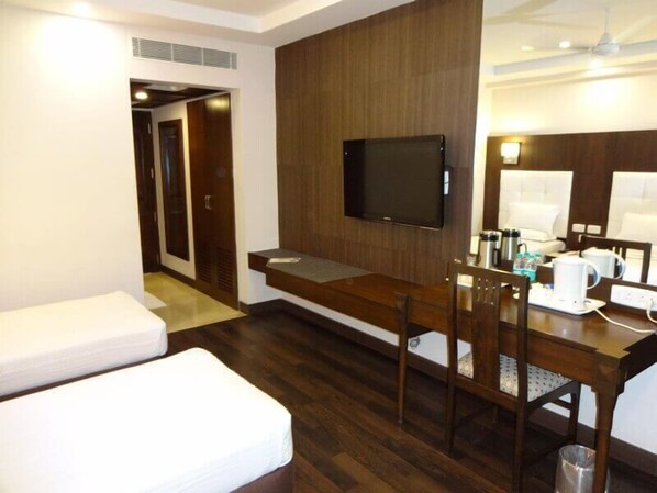 Habitación de hotel con escritorio de madera, televisión de pantalla plana, cama y pequeña mesa con cafetera.