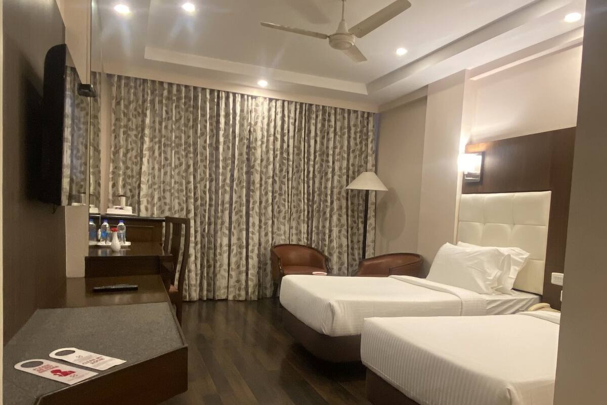 A hotel room with a bed, two chairs, a desk, a TV, and a ceiling fan.