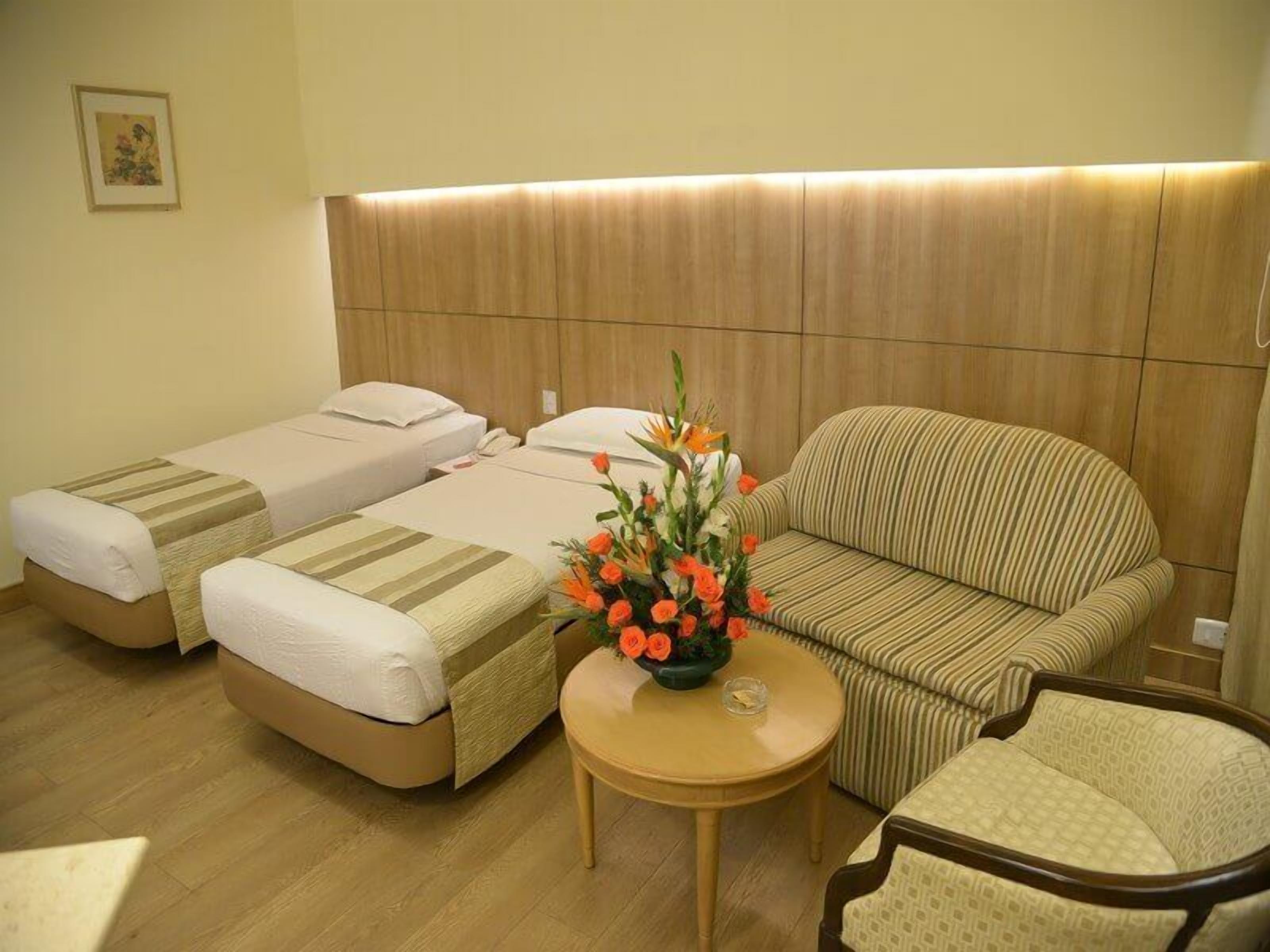 A hotel room with two single beds, a sofa, a small round table, and a flower arrangement.