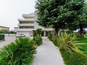 Un edificio moderno con entrada central, zona de estacionamiento y un jardín bien cuidado con diversas plantas.