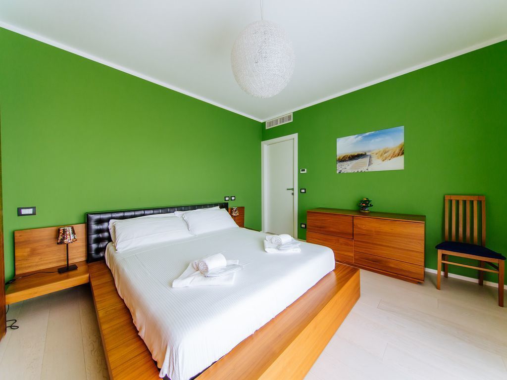 A bedroom with a large bed, a wooden dresser, a chair, and a painting on the wall.