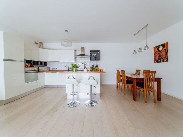 Una cocina moderna con armarios blancos, una isla central con taburetes y una zona de comedor con sillas de madera y una mesa.