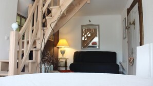 Una habitación con escalera de madera, cama, lámpara, espejo y puerta.