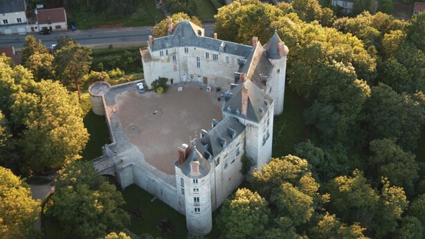 Vista aérea de un castillo con un amplio patio, rodeado de árboles frondosos.
