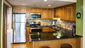 A kitchen with wooden cabinets, a stainless steel refrigerator, a microwave, an oven, a sink, and two bar stools. - 🌄Resort Vacations at Fairfield Glade TN Beautiful 2 bedroom Villa (Fairfield Glade)