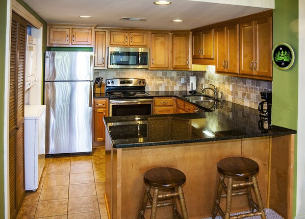 A kitchen with wooden cabinets, a stainless steel refrigerator, a microwave, an oven, a sink, and two bar stools.