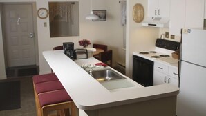 A compact kitchen with a white countertop, a sink, a stove, and a refrigerator. There is a dining area with a table and chairs, and a clock on the wall. - 'Best Deal in Telluride' - Walk to Gondola & lift 8!     TBL #00111 (Telluride)