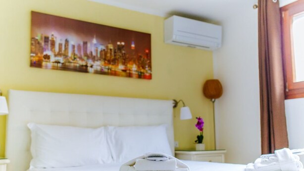 Een hotelkamer met een bed, een stadsgezichtschilderij, een airconditioner, een lamp en een raam met gordijnen.