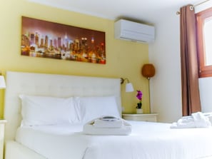 A hotel room with a bed, a cityscape painting, an air conditioner, a lamp, and a window with curtains. - Welc-oM Matilde (Padova)