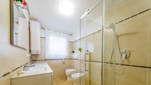 Een moderne badkamer met een douchecabine van glas, een wastafel en twee toiletten.