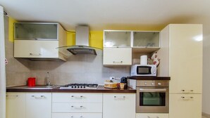 Een kleine keuken met een gasfornuis, magnetron, oven en een gele muur.
