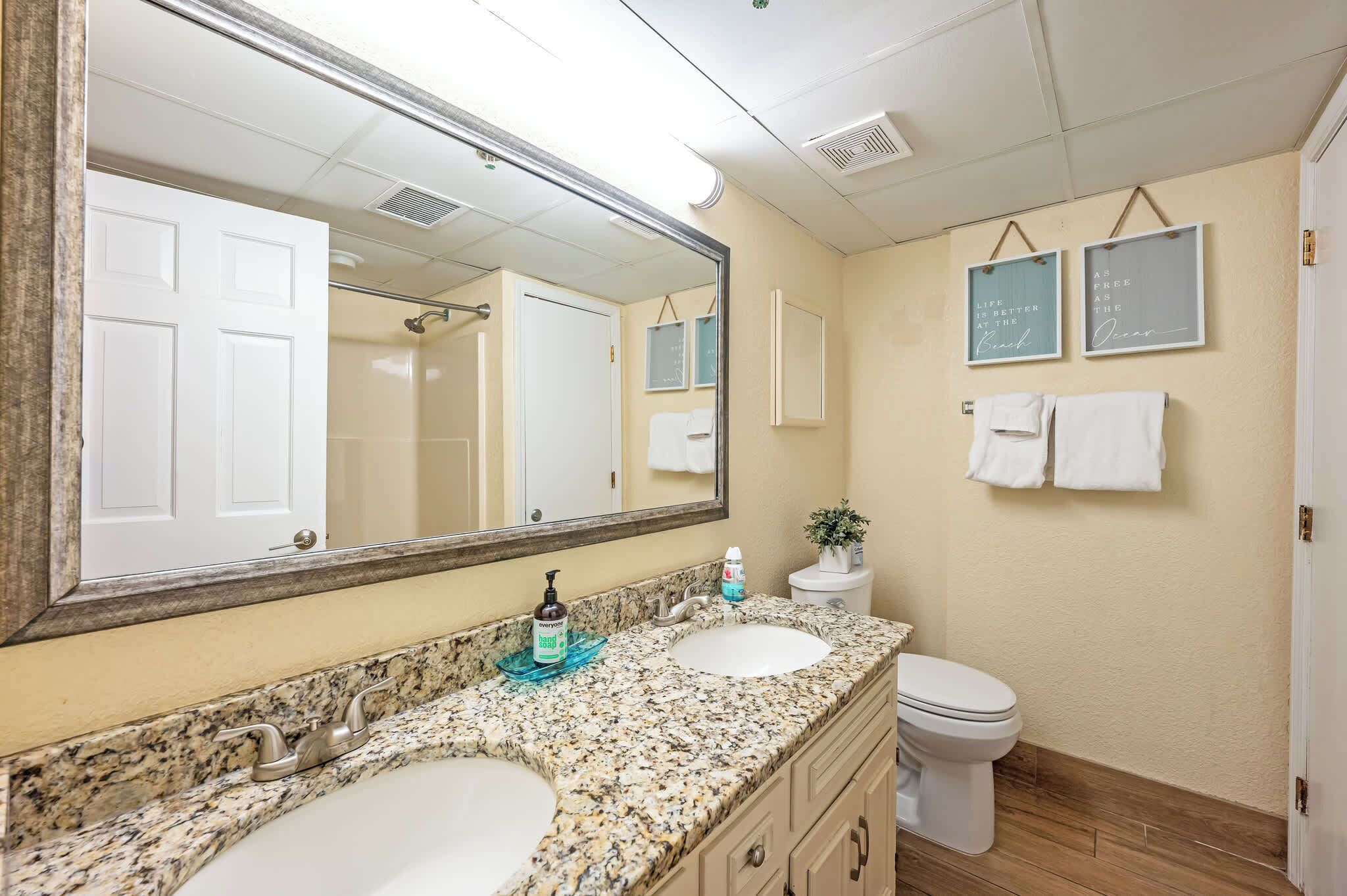 A bathroom with two sinks, a toilet, a large mirror, and two framed quotes on the wall.