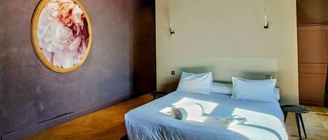 A modern bedroom with a large bed, a hanging light fixture, and a framed artwork on the wall.