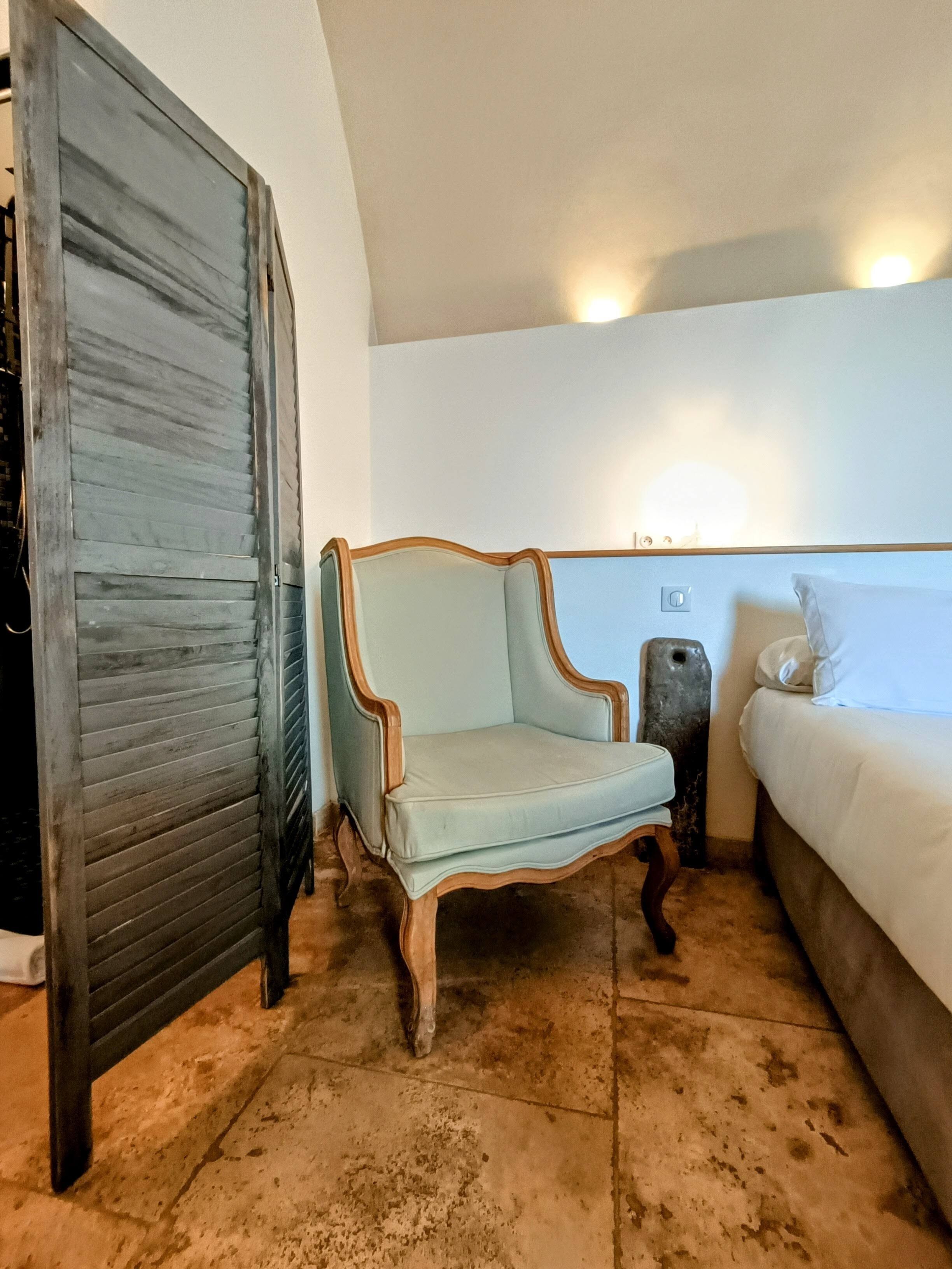 Ein Zimmer mit einem hellblauen Sessel, einem weißen Sofa und einem dunklen Holzschrank.