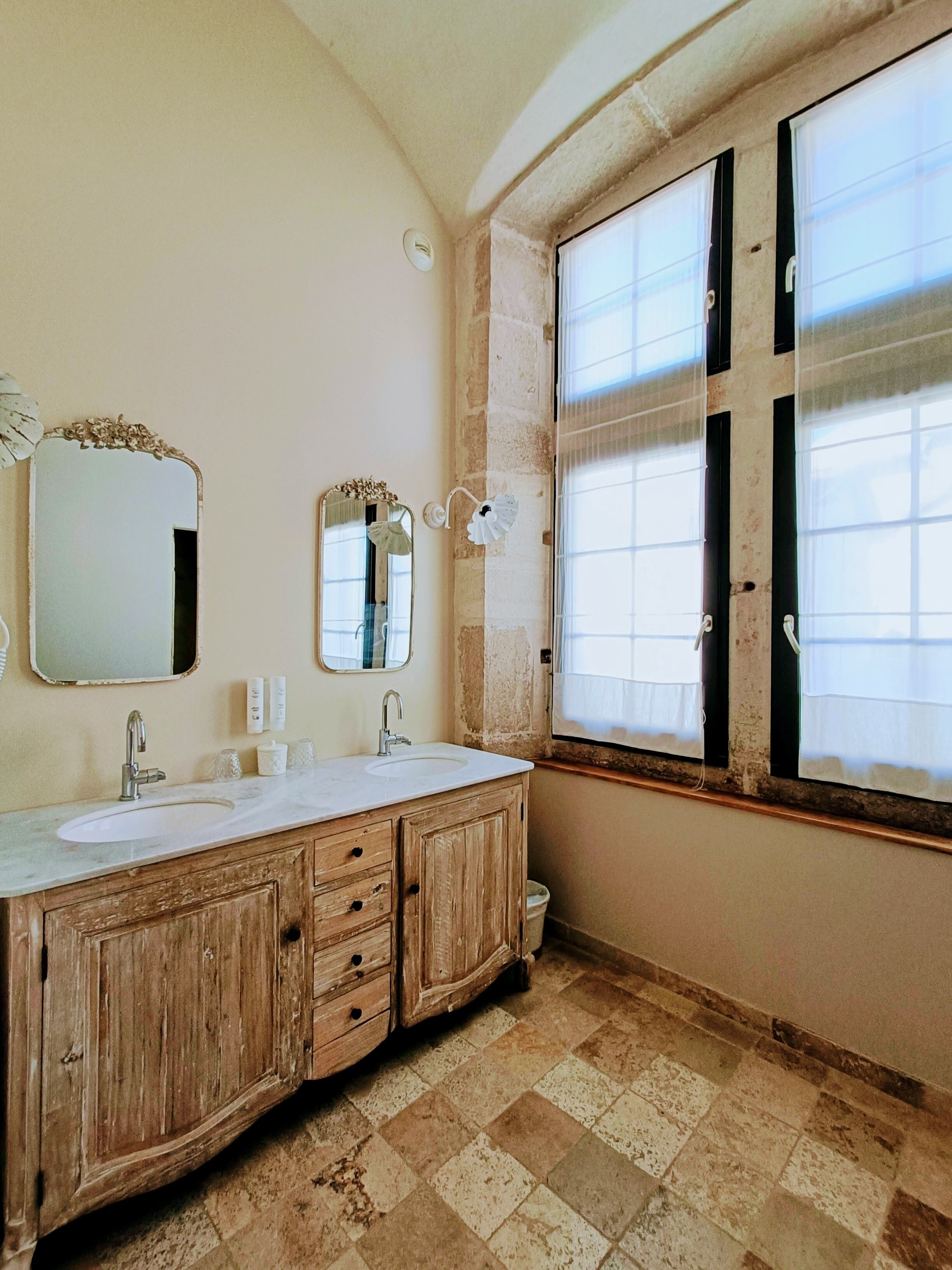 A bathroom with two sinks, wooden cabinets, a large mirror, and a window with blinds.