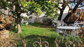 An outdoor seating area with metal tables and chairs, surrounded by trees and a stone wall.