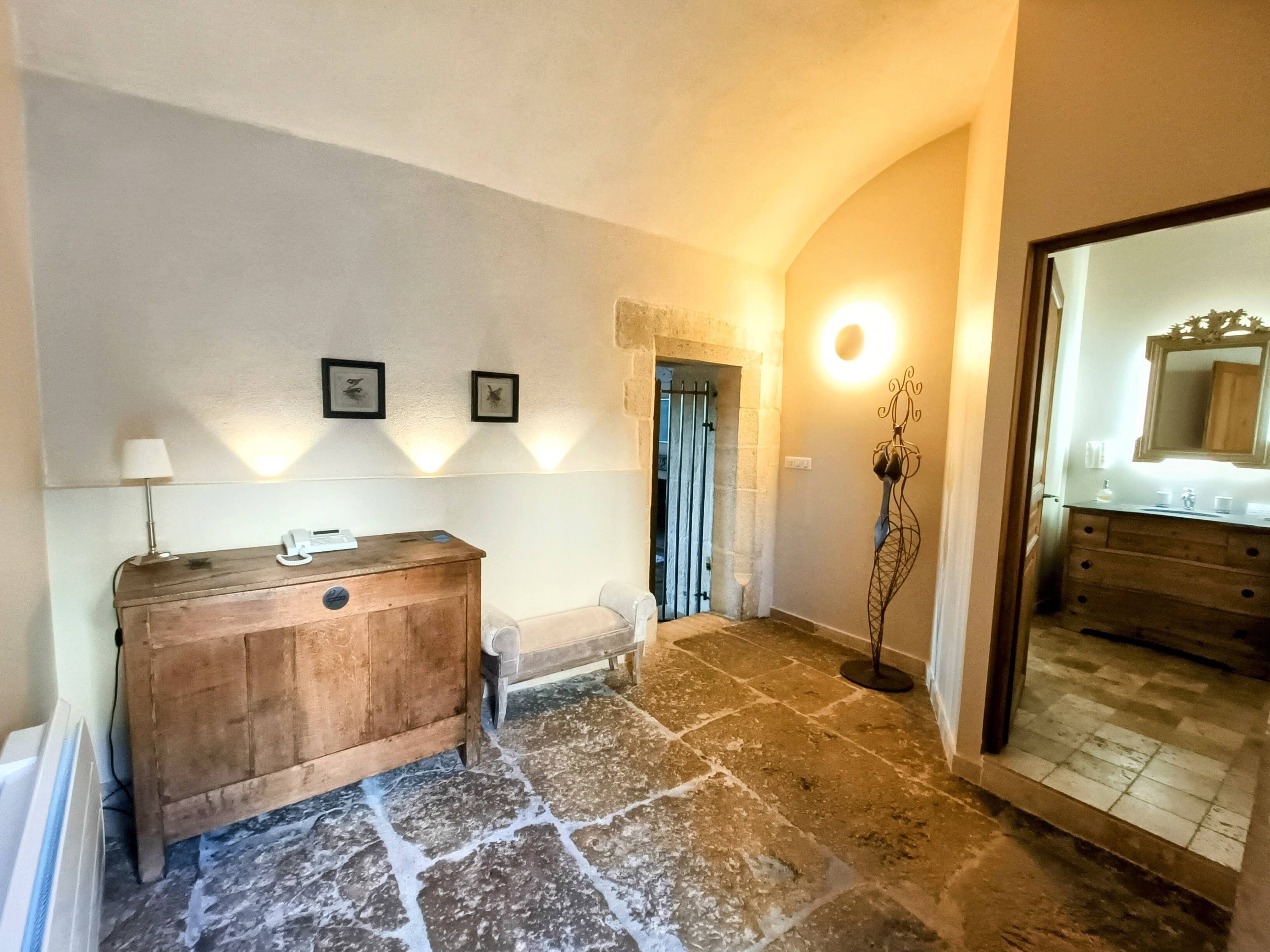 Un pasillo con un banco de madera, una mesita con lámpara, cuadros enmarcados en la pared y un espejo con marco decorativo.