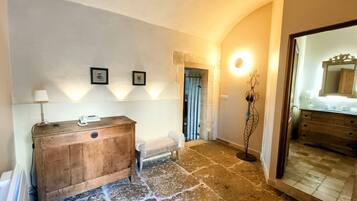 Un pasillo con un banco de madera, una mesita con lámpara, cuadros enmarcados en la pared y un espejo con marco decorativo.