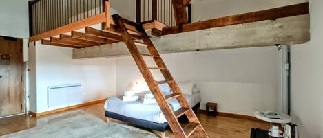 A loft bedroom with a wooden ladder, a bed, a small table, and a television.