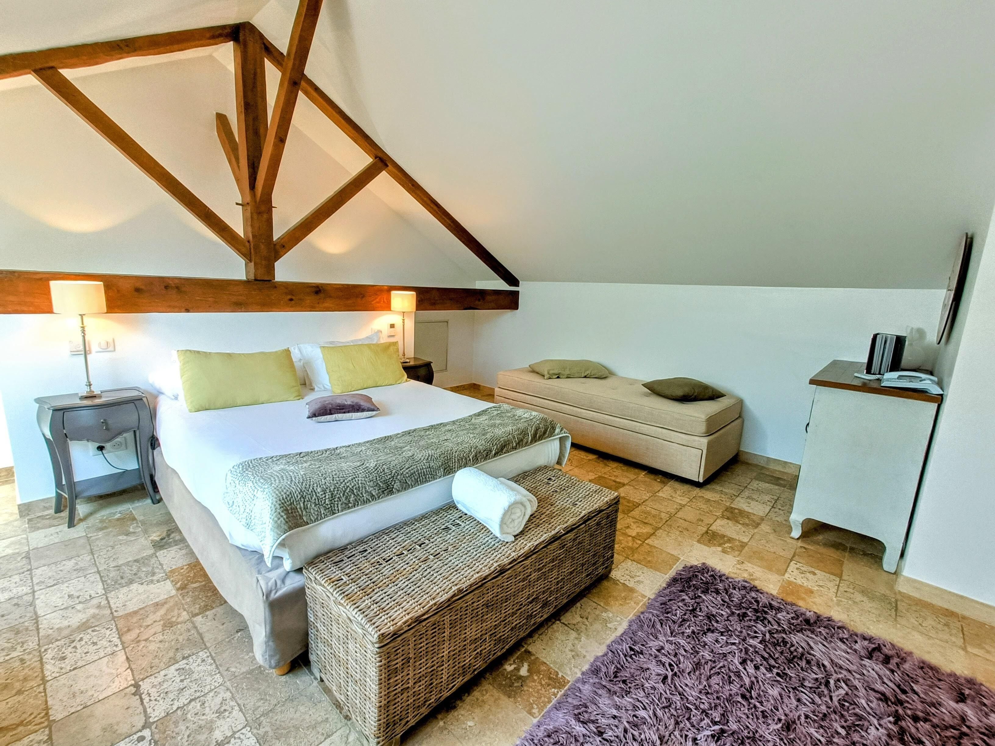 A bedroom with a large bed, a bedside table with a lamp, a bench, and a small cabinet.