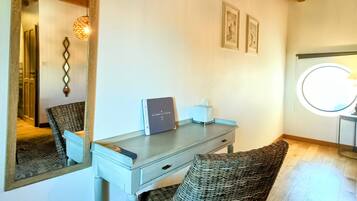 Ein Zimmer mit Schreibtisch, Stuhl, Spiegel, gerahmten Bildern und einem Deckenventilator.