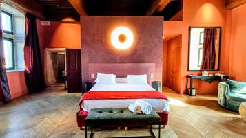 A hotel room with a large bed, a bench, a circular light fixture, and a wooden ceiling.
