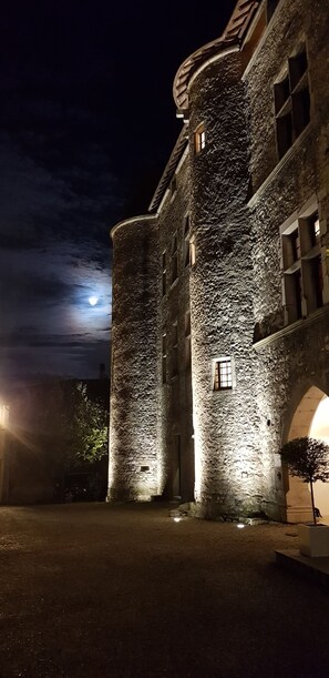 A stone building with a round tower at night, illuminated by artificial lighting. - Les Chambres De La Renaissance (Sainte-Julie)