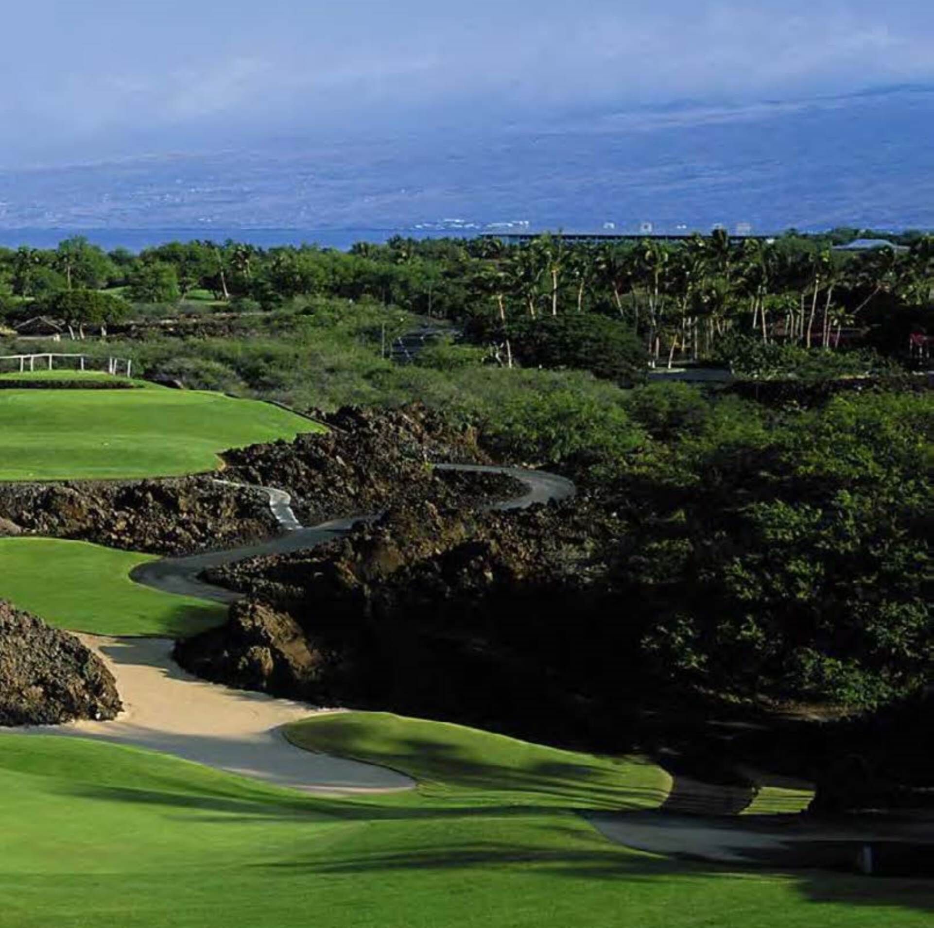 Un campo de golf con un sendero sinuoso, césped verde exuberante y terreno rocoso.