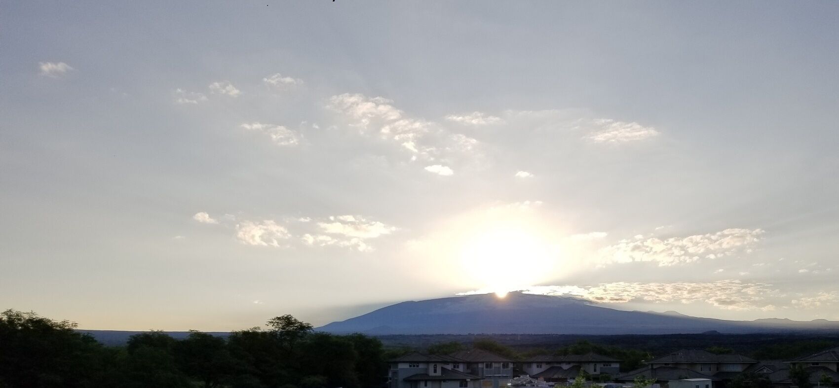 Une montagne, avec le soleil se couchant derrière elle, projetant une lumière dorée sur le paysage.